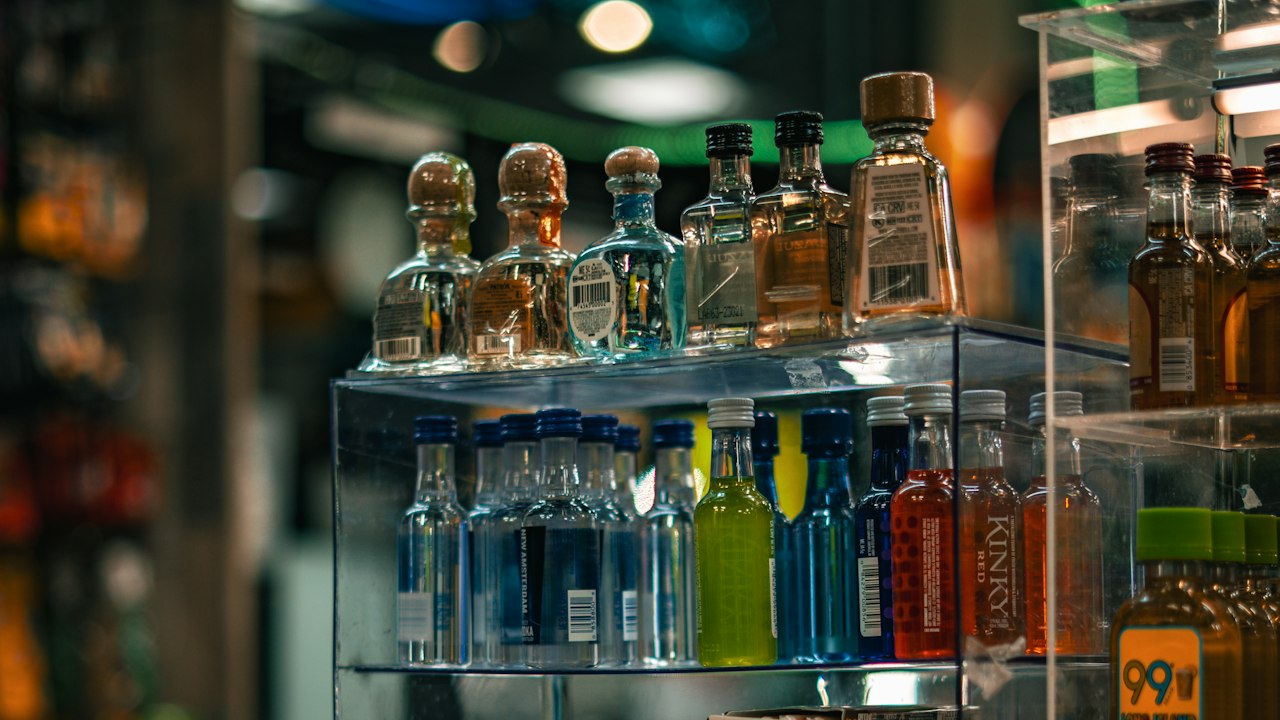A glass display vitrine stocked with liquor bottles and boxed goods, softly lit