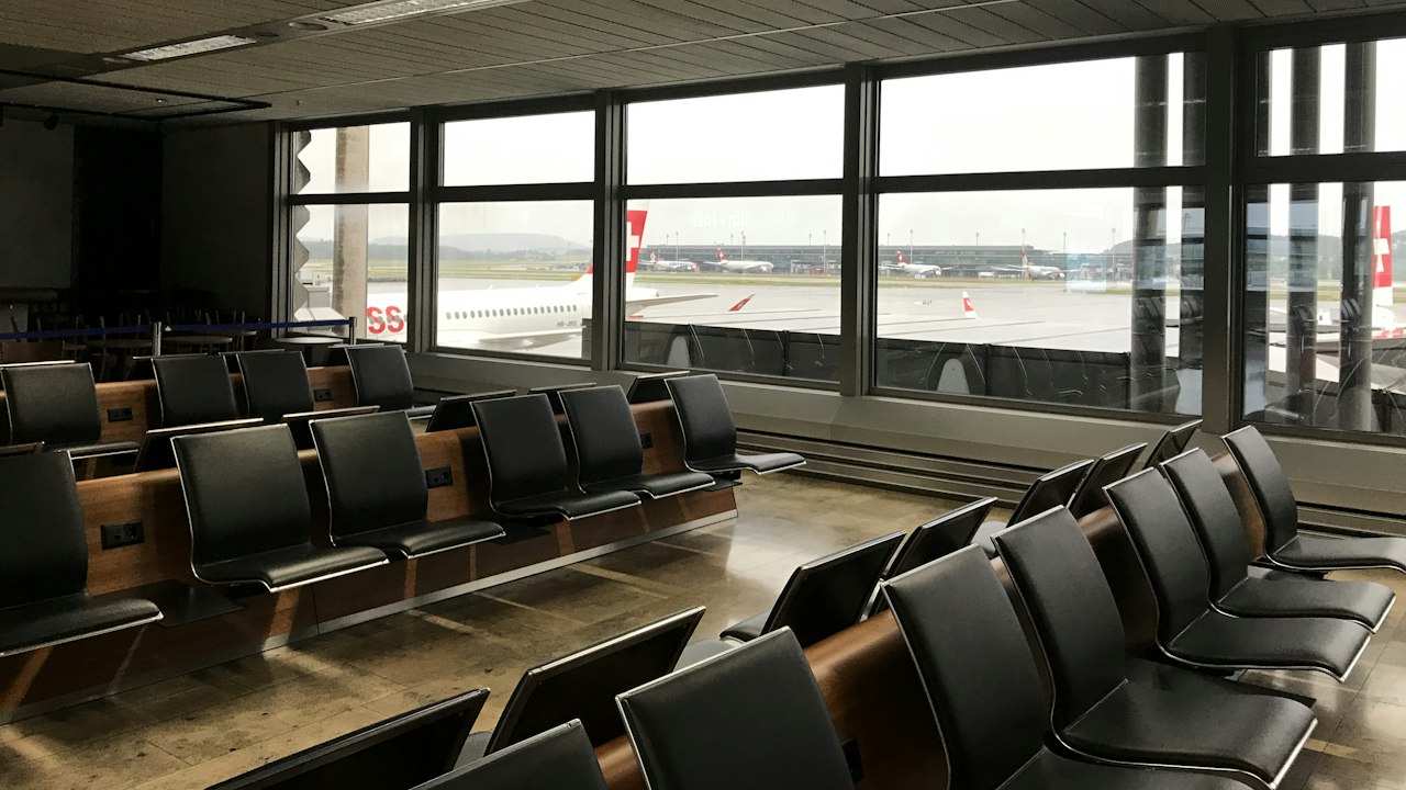 An airport gate waiting area with rows of dark seats facing tall windows