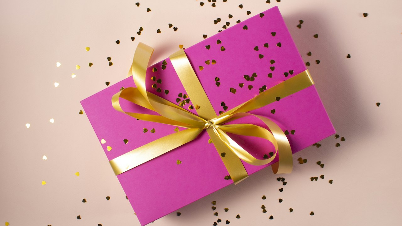 A wrapped gift box with a gold ribbon bow on a soft pink background